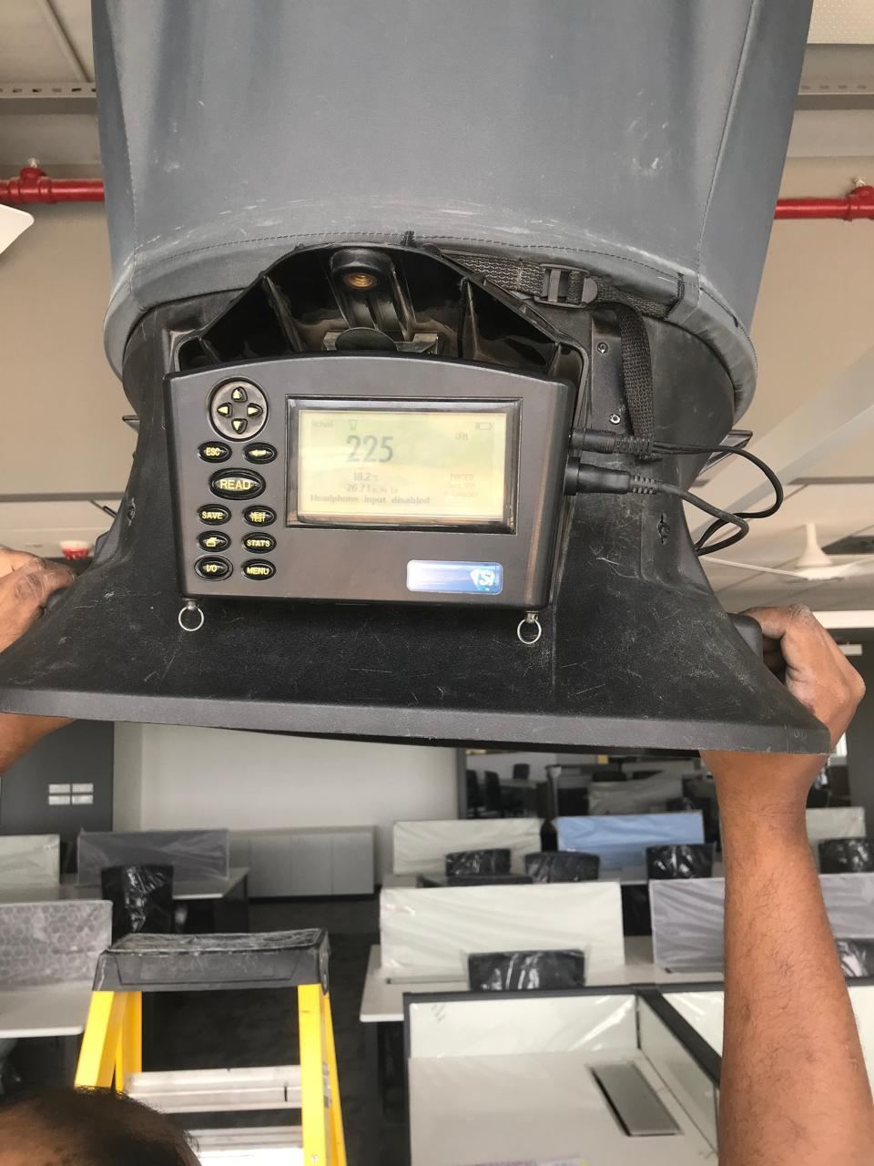Air balancing measurement being taken at a duct outlet using a flow hood